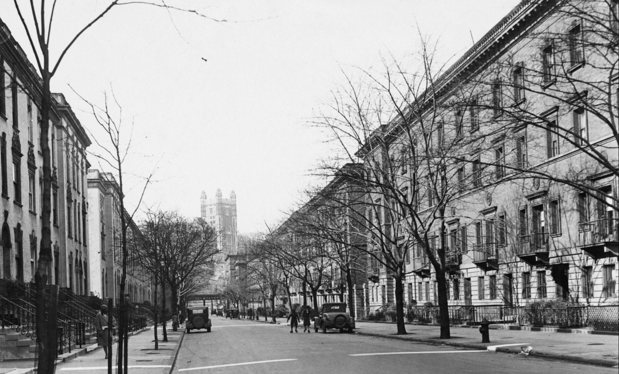 A view down a street in Harlem, New York City, with the tower of the College of the City of New York in the background, circa 1930.